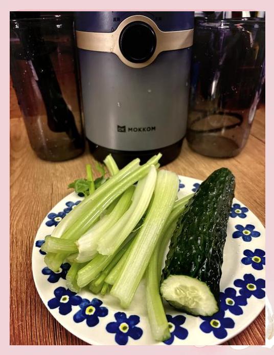 一位女性正在使用慢速榨汁机制作绿色果蔬汁，操作台上有切好的黄瓜和西芹