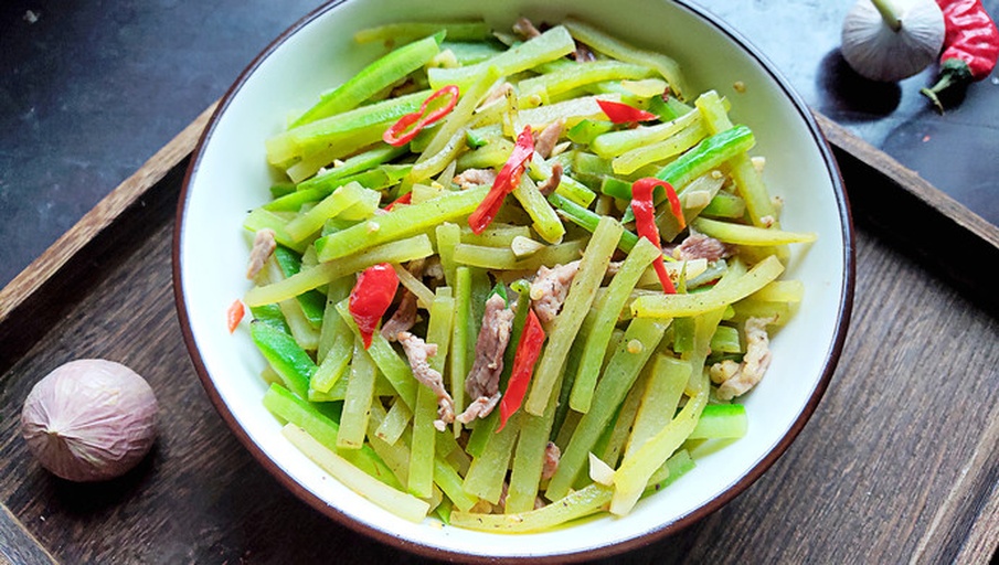 一盘刚出锅的清炒尖叶莴笋叶,色泽翠绿,油光适中,配有几片红椒丝点缀,盛放在白色瓷盘中,摆放在木质餐桌上,体现健康家常菜肴风格 清炒尖叶莴笋叶成品图