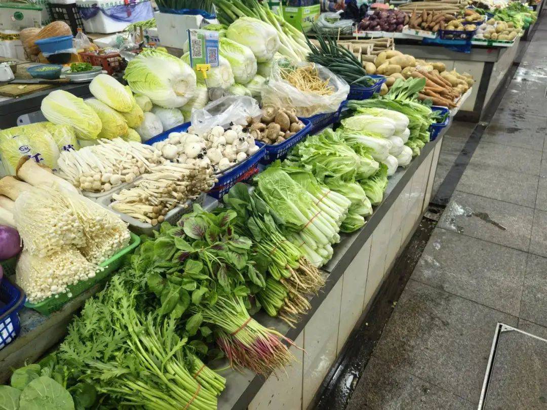 一个传统菜市场摊位,陈列着多种绿叶蔬菜,包括油菜、小白菜和芥菜,摊主正在整理菜品,背景有手写价格牌,突出‘油菜’字样 菜市场摊位上的绿叶蔬菜特写