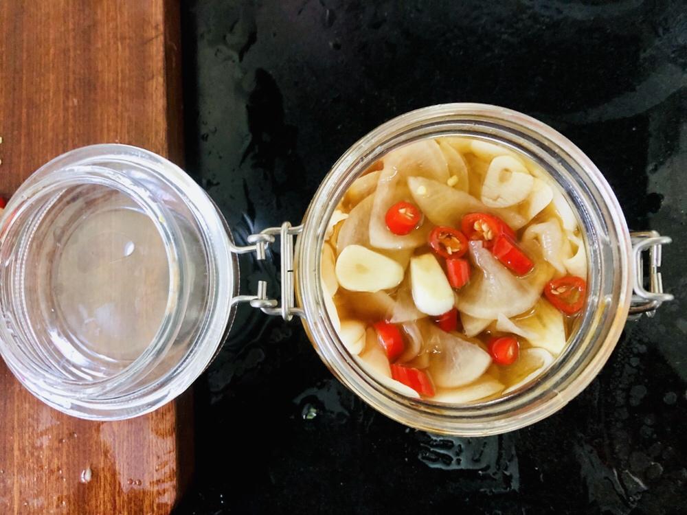 玻璃密封罐中装着粉红色的腌萝卜条,浸泡在透明液体中,旁边摆放着切好的蒜片和小米辣,桌面上散落着几片新鲜萝卜叶 玻璃密封罐中装着粉红色的腌萝卜条,浸泡在透明液体中,旁边摆放着切好的蒜片和小米辣,桌面上散落着几片新鲜萝卜叶