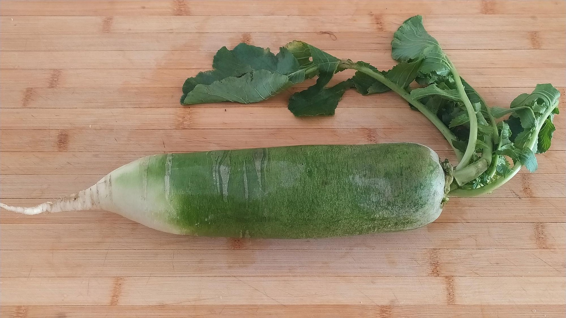 一根新鲜的青萝卜,表皮呈青绿色渐变至白色,切开后露出洁白多汁的内部组织,表面有细微水珠,背景为木质砧板和绿叶点缀,展示其自然清新的农产品特质 青萝卜特写