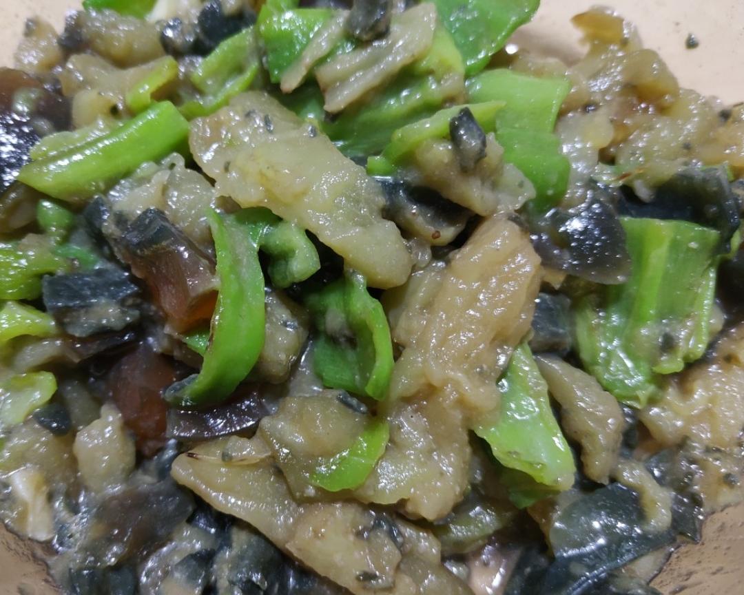 厨师正在使用石制擂钵捣制线椒茄子擂皮蛋，手中木槌正压在线椒与蒜末混合物上，食材呈现半糊状，周围可见撕好的茄子条与切块皮蛋
