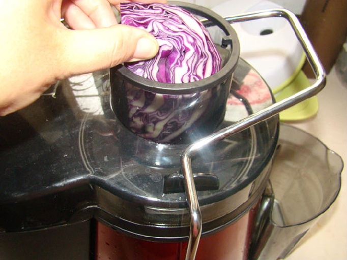 一名厨师正在将新鲜紫甘蓝切碎后放入榨汁机中榨取紫色汁液,另一碗中为白色面粉,旁边是一盆揉好的淡紫色面团,展示从原料到和面的过程 紫甘蓝榨汁与面团混合过程