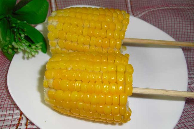 餐桌上摆放蒸煮后的金黄色甜玉米棒,旁边配有切片摆盘、玉米沙拉、奶油玉米汤等多种创意吃法,展现甜玉米的多样化食用场景 东北甜玉米烹饪与餐桌呈现方式