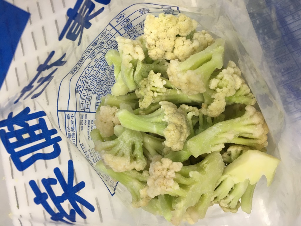 一名厨师正在将切好的韭菜花平铺在金属托盘上,准备放入冰箱冷冻;旁边有密封袋、厨房纸和标签笔,展示完整的冷冻准备流程 韭菜花冷冻处理过程图