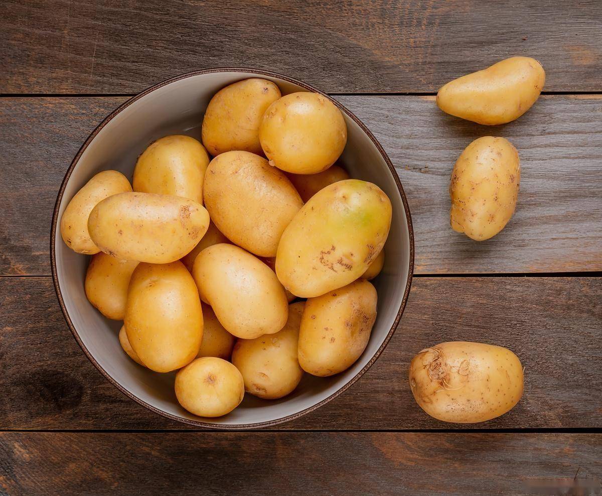 白色瓷碗中盛放加热后的整颗小土豆,搭配新鲜生菜、番茄片和橄榄油调味,整体呈现健康轻食风格,背景为木质餐桌和自然光 餐桌上一碗热气腾腾的复热蒸土豆配蔬菜沙拉