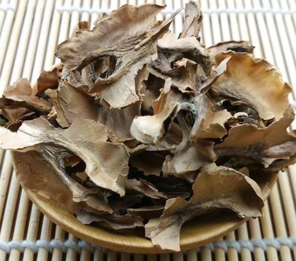 一盘干燥的核桃分心木,呈网状结构,颜色为浅棕至深褐色,碎片大小不一,背景为木质砧板,旁边放置一颗完整带壳核桃作为参照物 核桃分心木实物特写