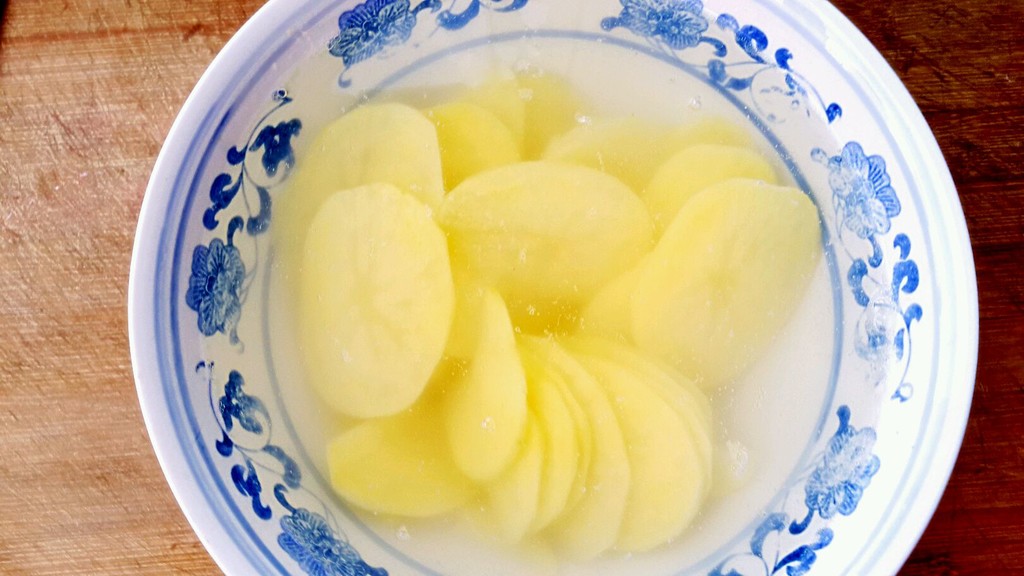 一盘切好的土豆条浸泡在透明玻璃碗的清水中,水面略高于土豆,背景为厨房操作台,光线自然柔和,体现家庭食材处理场景 图片描述