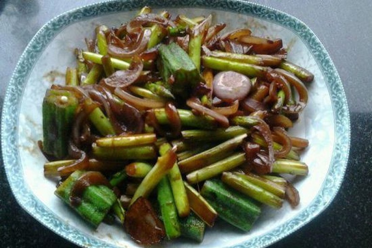 炒锅中正在翻炒秋葵与洋葱，食材呈现金黄色光泽，蒜末清晰可见，热气腾腾