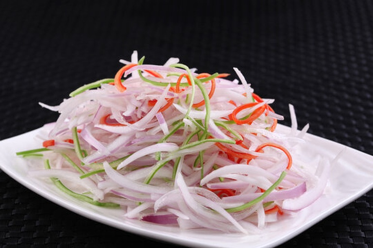 一个白色瓷盘中盛放着由紫皮洋葱薄片、红黄彩椒丝、樱桃番茄和芝麻菜组成的混合沙拉,洋葱片呈现半透明紫色,表面淋有光泽的橄榄油,撒有黑色芝麻点缀,旁边放有一块柠檬角,整体色彩鲜艳,体现健康饮食风格 紫皮洋葱制作的健康沙拉盘