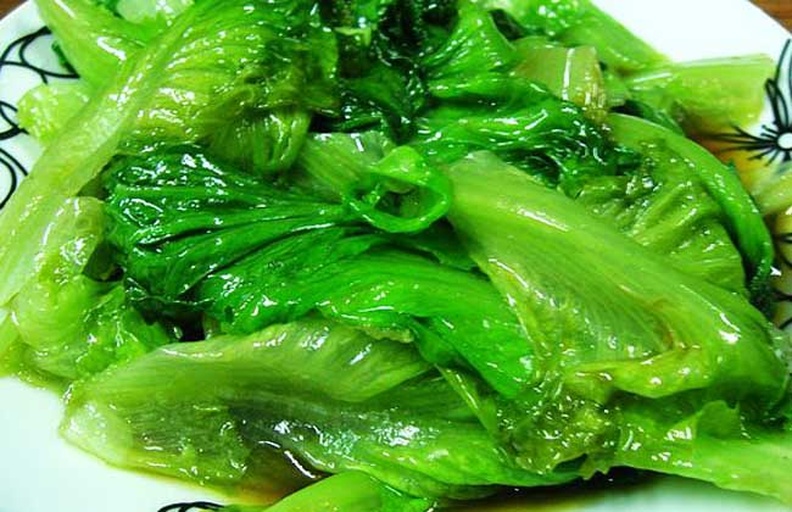 一盘刚出锅的清炒生菜,颜色翠绿鲜亮,表面泛着微微油光,盘中可见完整的叶片和金黄色的蒜末点缀,背景为木质厨房台面 清炒生菜出锅图