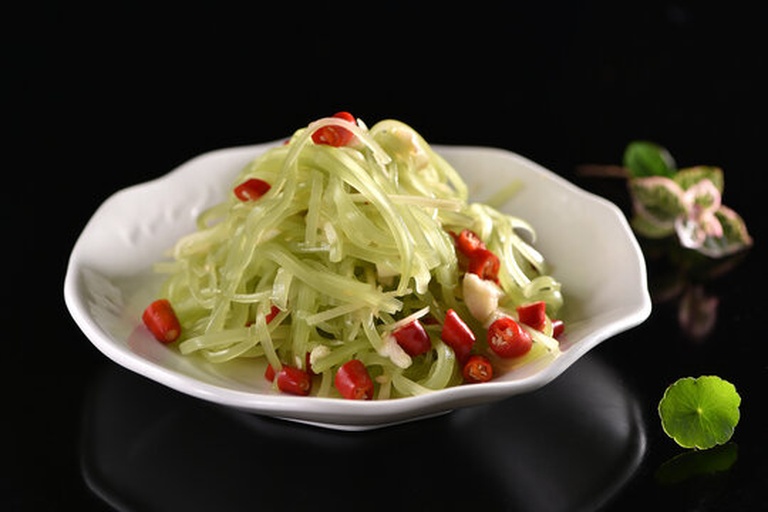 一盘精致的凉拌山芹菜肴,颜色翠绿,搭配红椒丝和蒜末点缀,盛放在白色瓷盘中,表面淋有少量透明调味汁,呈现清新健康的视觉效果 凉拌山芹成品图