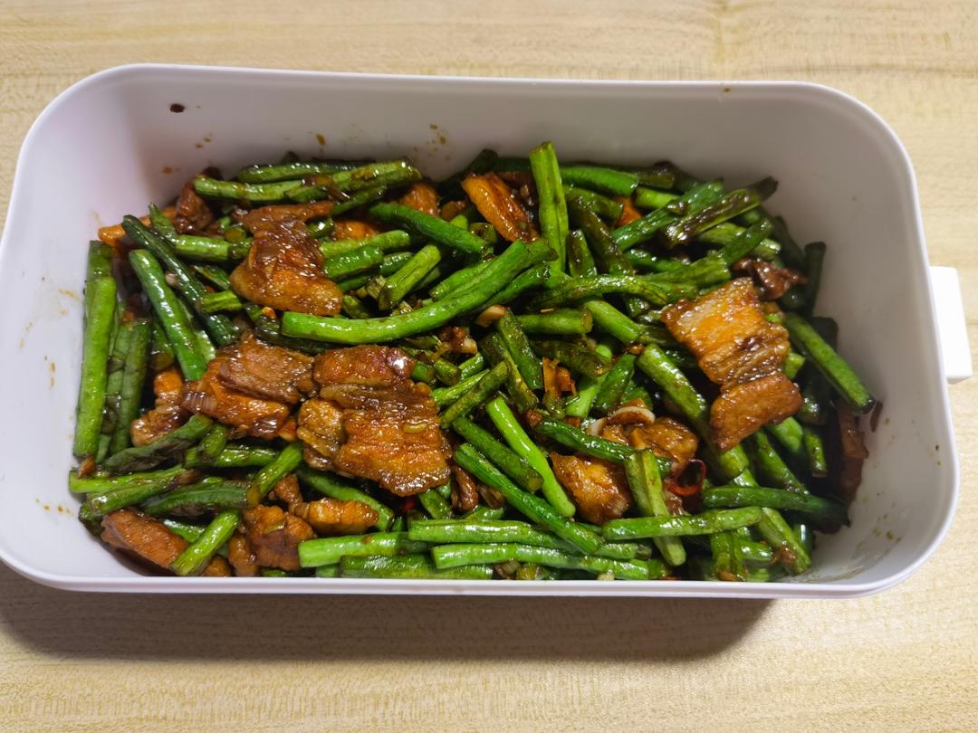 干香诱人的豆角五花肉小炒:深褐色五花肉片微卷,翠绿豆角段裹着红亮酱汁,表面点缀数粒金黄干辣椒和花椒,热气氤氲,盛于青花瓷浅盘中,木纹餐桌背景 豆角五花肉干煸成品图