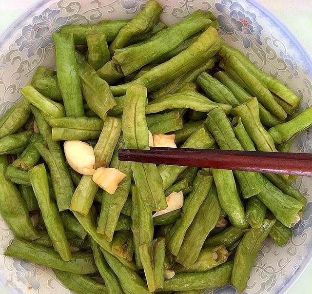 白色瓷盘中盛放着刚出锅的豆角炒蒜苔,颜色翠绿明亮,表面泛着油光,点缀少许红椒丝和蒜片,旁边配有木筷和一碗米饭,呈现温馨家常氛围 成品豆角炒蒜苔摆盘效果