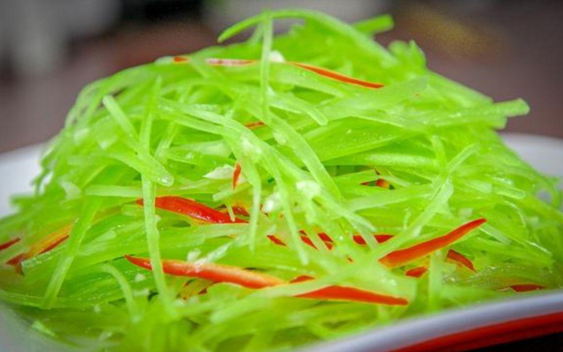 一盘装盘精美的凉拌莴苣成品，翠绿莴苣丝整齐码放，撒有白芝麻和红辣椒圈，盛于白色瓷盘中