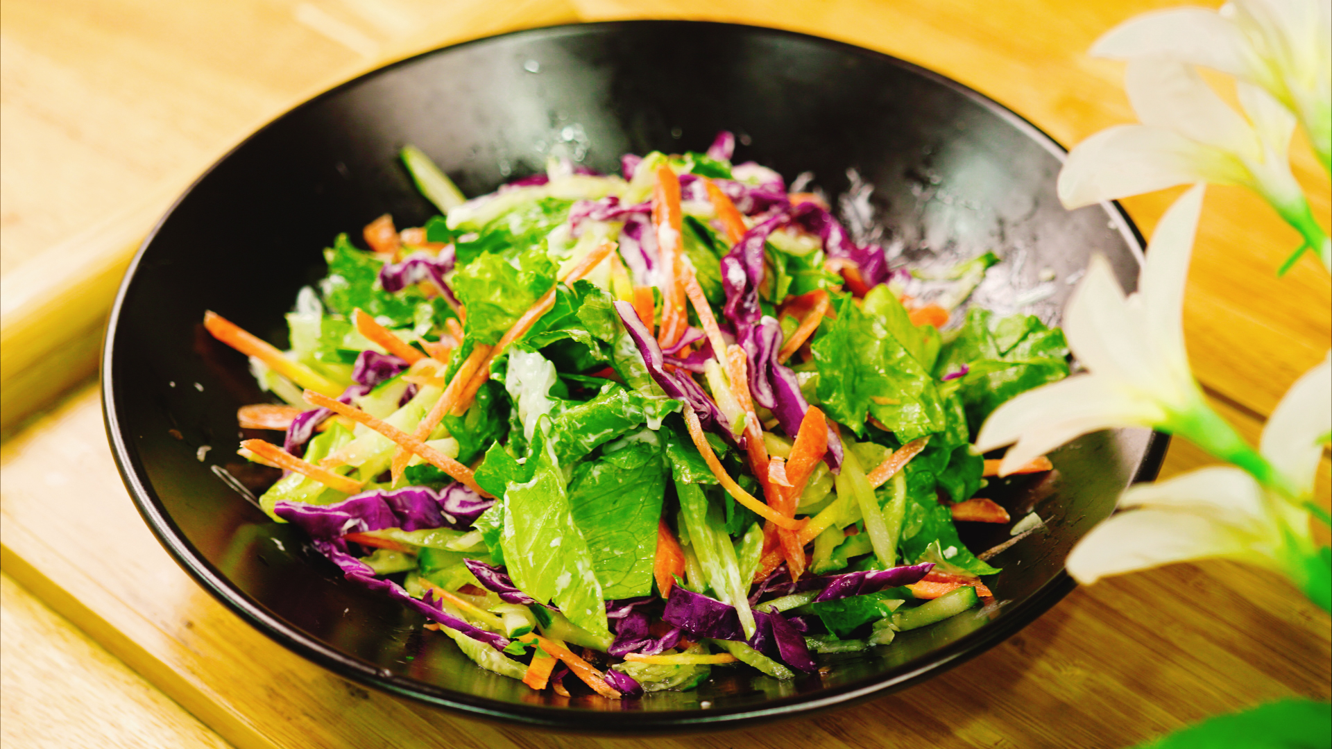 一个白色瓷碗中盛满色彩丰富的沙拉,包含罗马生菜、红橡叶生菜、紫甘蓝丝、小番茄、黄瓜片、煮鸡蛋和烤鸡胸肉丁,表面淋有少量透明油质酱汁,整体呈现健康轻食风格,背景为木质餐桌 混合沙拉碗