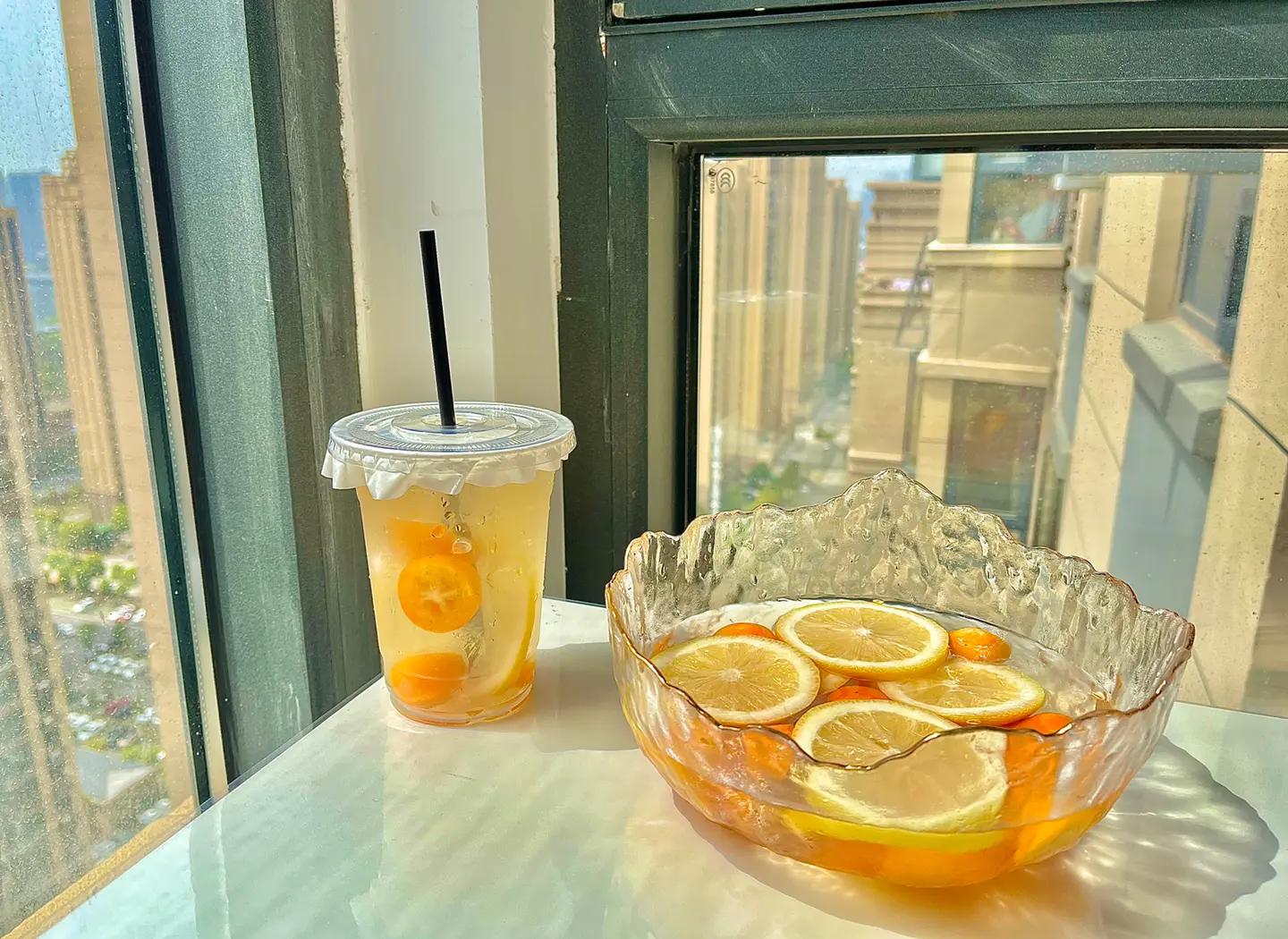 一杯透明玻璃杯中浸泡着两颗金桔,水中漂浮着柠檬片和薄荷叶,背景为厨房台面,阳光洒入,营造健康生活方式氛围 金桔茶饮场景图