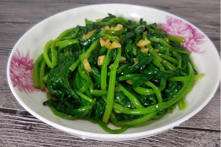 一盘已经烹饪好的蒜蓉炒小叶菠菜,盛放在白色瓷盘中,叶片翠绿油亮,表面覆盖着金黄色的蒜粒,整体看起来香气扑鼻,旁边配有米饭和筷子,营造出温馨家常用餐氛围 小叶菠菜料理成品图