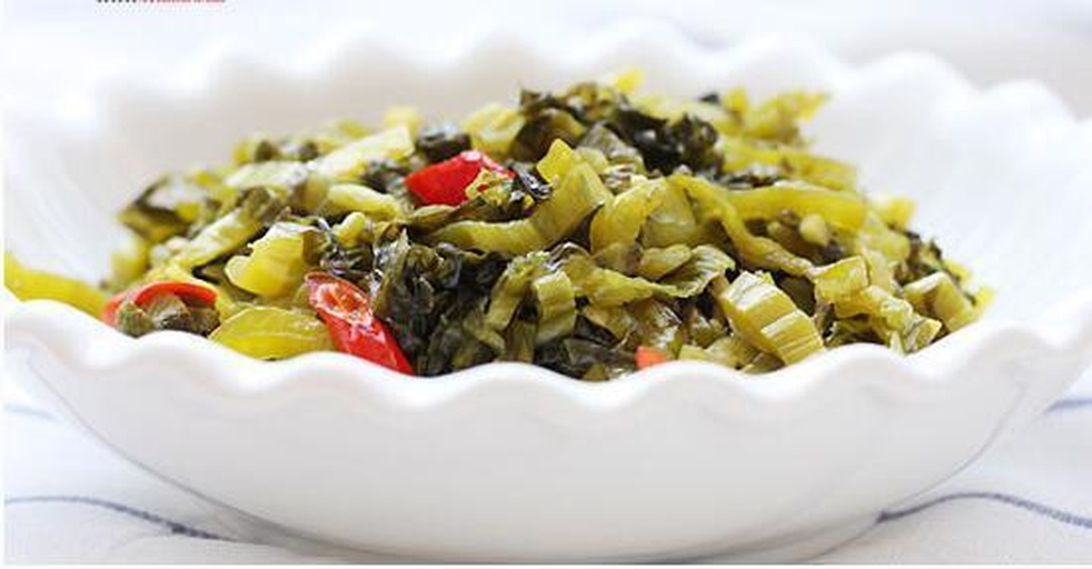 一张木质餐桌上摆着一碗金黄色的酸菜炖肉,旁边是一盘刚出锅的酸菜饺子和一小碟辣椒油,前景有一小坛揭开盖子的酸菜缸,可见内部整齐码放的黄色酸菜,整体呈现温暖农家风味氛围 酸菜成品与菜肴搭配展示