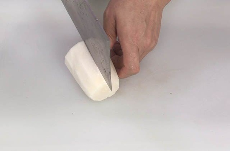 一位厨师正在灶台前翻炒锅中的白萝卜片,锅中热气腾腾,萝卜已微微透明,旁边案板上有切好的新鲜白萝卜和葱姜配料,厨房环境整洁明亮,体现家庭烹饪的真实感 厨房中正在烹饪白萝卜菜肴的场景