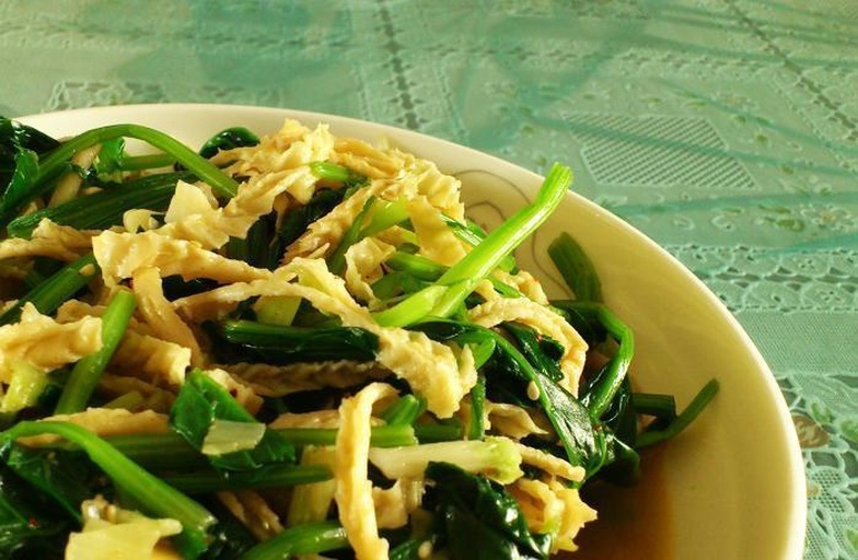 新鲜绿叶菠菜与干燥金黄色豆皮并列摆放于木质砧板上,背景为厨房环境,光线柔和自然,突出两种食材的色泽与质感 菠菜与豆皮食材特写