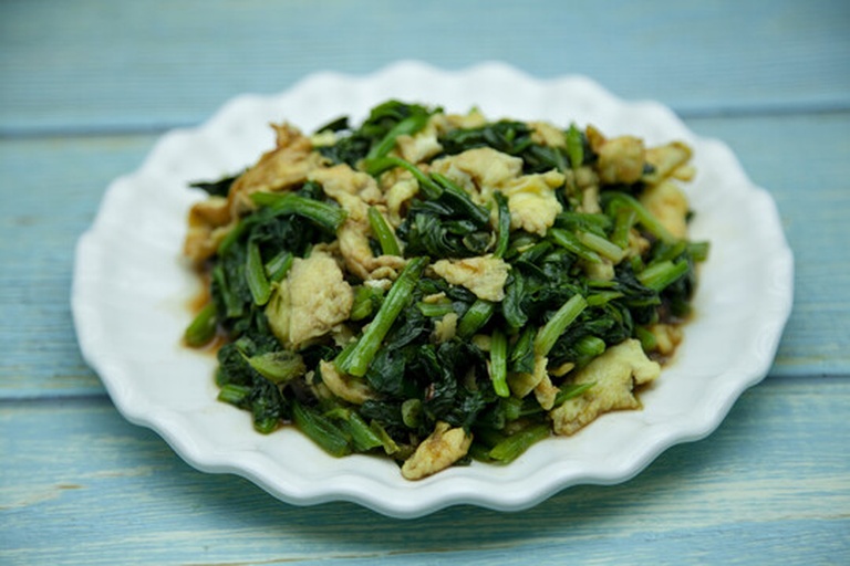 一盘金黄色与翠绿色交织的菠菜炒蛋菜肴,盛放在白色瓷盘中,表面微带油光,可见清晰的蛋块与菠菜段,展现家常菜的色香味俱全 菠菜炒蛋成品特写图