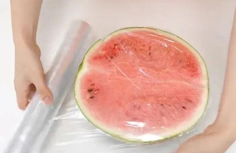 切开的西瓜块整齐码放在透明玻璃保鲜盒中，红瓤黑籽分明，表面覆盖严实食品级保鲜膜，盒子置于冰箱冷藏室中层搁架