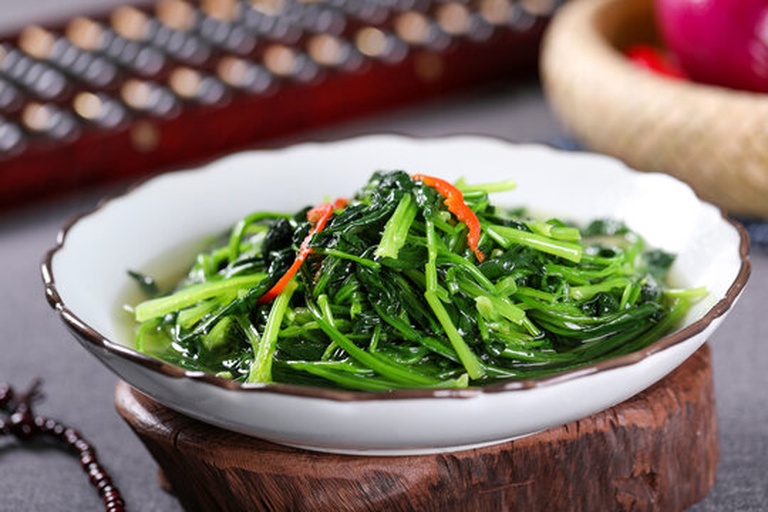 一盘精致摆盘的八宝菠菜,中央为整齐码放的大叶菠菜,周围环绕着色彩缤纷的八种配料:红色胡萝卜丁、黑色木耳碎、黄色鸡蛋丝、浅粉色火腿粒、乳白莲子、棕褐色核桃仁、绿色豌豆和透明粉丝段,整体呈放射状布局,撒有少量白芝麻点缀,使用白色瓷盘盛装,背景为木质餐桌与竹筷 八宝菠菜成品特写