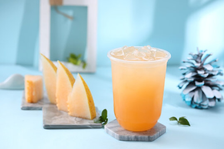 一杯盛装好的哈密瓜果汁,背景清新,突出果汁的色泽与冰块 哈密瓜果汁成品展示