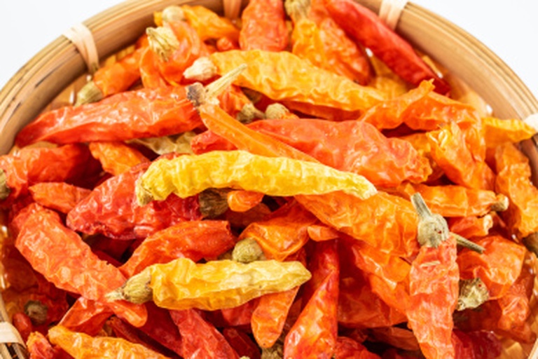 干辣椒加工场景：木质案板上铺展着不同形态干辣椒——整颗灯笼椒、剪段朝天椒、研磨中的辣椒碎，旁边配有铜制石臼与木杵，背景为暖光照射的传统川西农家厨房