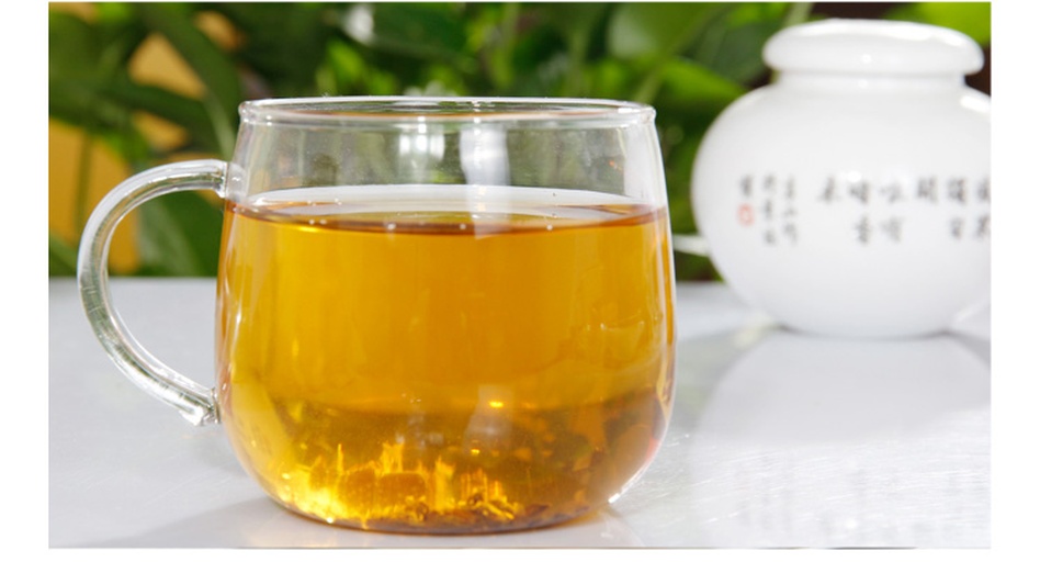 图片说明:透明玻璃杯内盛有浅琥珀色茶汤,水中悬浮着数粒黑色苦荞碎块和两片红褐色山楂薄片,部分山楂已吸水膨胀。杯子置于白色陶瓷碟上,背景模糊,聚焦于液体色泽与内容物分布状态 玻璃杯中浸泡的苦荞山楂水特写