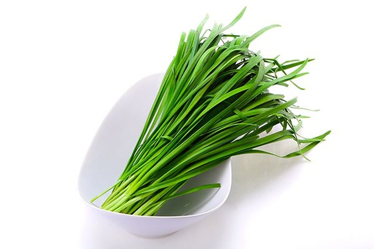 家庭厨房场景中，厨师正在将切碎的韭菜加入凉拌菜中，准备一道护肝营养餐