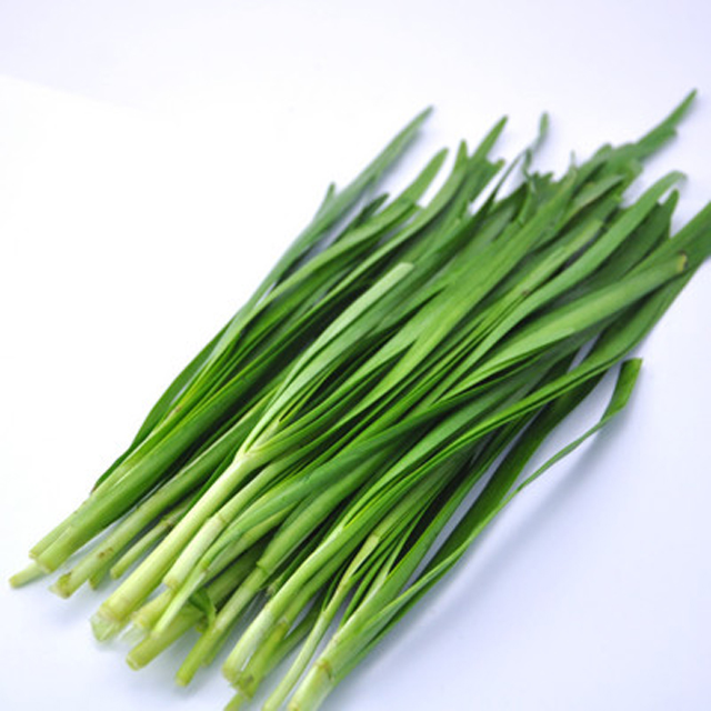 一张高清实拍图,左侧为一把翠绿的新鲜韭菜,根部带泥,叶片细长扁平;右侧为一小堆干燥的黑色韭菜籽,颗粒细小呈卵圆形,表面光滑有光泽。背景为木质案板,整体风格自然、贴近农家食材场景 韭菜与韭菜籽实物对比图