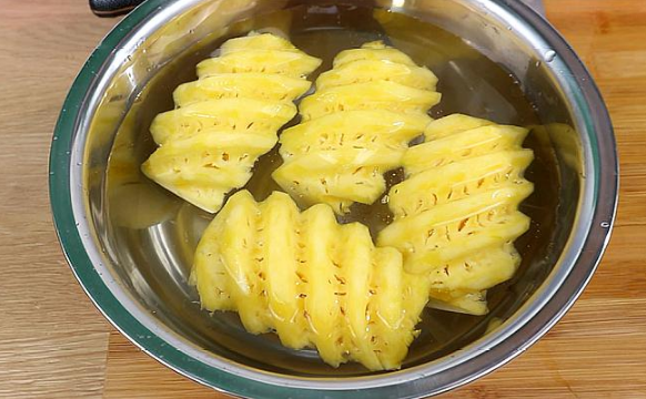 左侧为刚切好的新鲜菠萝块(金黄色、表面光洁、汁液清亮);右侧为同一品种菠萝块在4℃纯净水中浸泡12小时后的状态(颜色转为浅褐黄、表面出现微黏液、底部有少量絮状沉淀;容器内水质明显浑浊,可见细小气泡附着于果肉表面 菠萝切块在玻璃容器中浸泡水样对比图