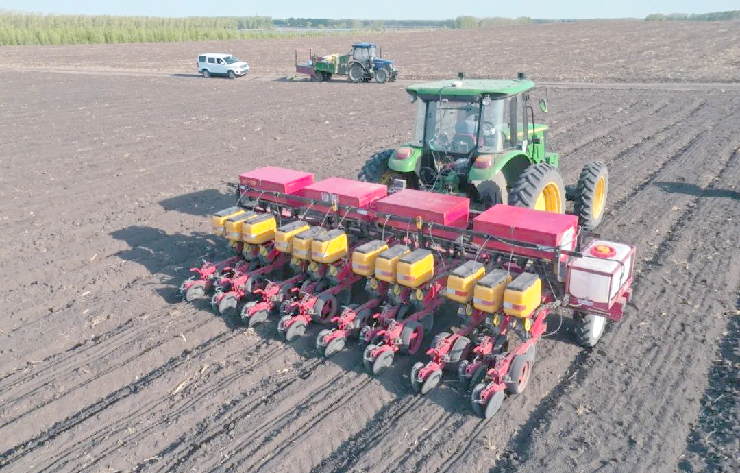 农民在田间进行油菜机械化播种作业,拖拉机牵引播种机前行,土地平整湿润,种子均匀播撒,展现现代化油菜种植流程 油菜播种与田间管理场景