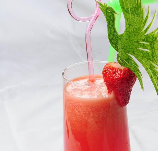 一杯刚做好的草莓香蕉牛奶特写,液体呈现柔和的粉橙色调,杯子外壁有冷凝水珠,顶部装饰有新鲜奶油草莓切片和绿色薄荷叶,背景虚化 手持玻璃杯中的粉橙色饮品,杯壁凝结水珠,上方漂浮着半片奶油草莓和薄荷叶