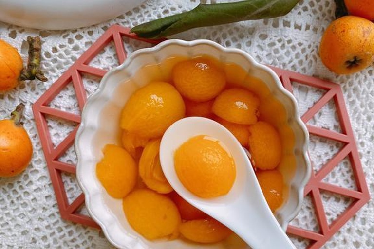 现代化食品工厂内景,透明玻璃后是全自动化的枇杷汁生产线:包括清洗机、去皮去核机组、螺旋压榨机、膜过滤装置和无菌灌装设备;不锈钢管道闪着光泽,工人正在操作控制面板监控参数,传送带上整齐排列着待装瓶的玻璃瓶装枇杷汁 现代化枇杷汁生产线