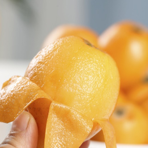 新鲜剥皮的枇杷摆放在白色瓷盘中，果肉呈橙黄色，表面光滑湿润，背景为浅木色餐桌，旁边有半颗未剥皮的枇杷作为对比