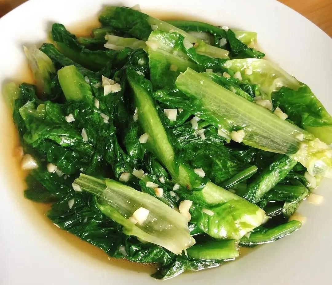 生菜茎部快炒工艺实拍:斜切茎片在低温蒜油中快炒70秒,呈现半透明脆嫩质地,与生食叶片形成营养互补搭配 生菜茎部斜切薄片与蒜末在铁锅中快炒特写,油光润泽,茎片呈半透明脆感,背景可见未烹饪的翠绿叶片