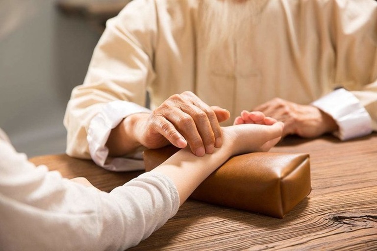 一位身穿白大褂的中医师在诊所内与中年患者面对面交流,桌上摆放中药柜、脉枕和一杯山楂水,墙上挂着经络图,营造专业医疗咨询氛围 中医师与患者咨询场景