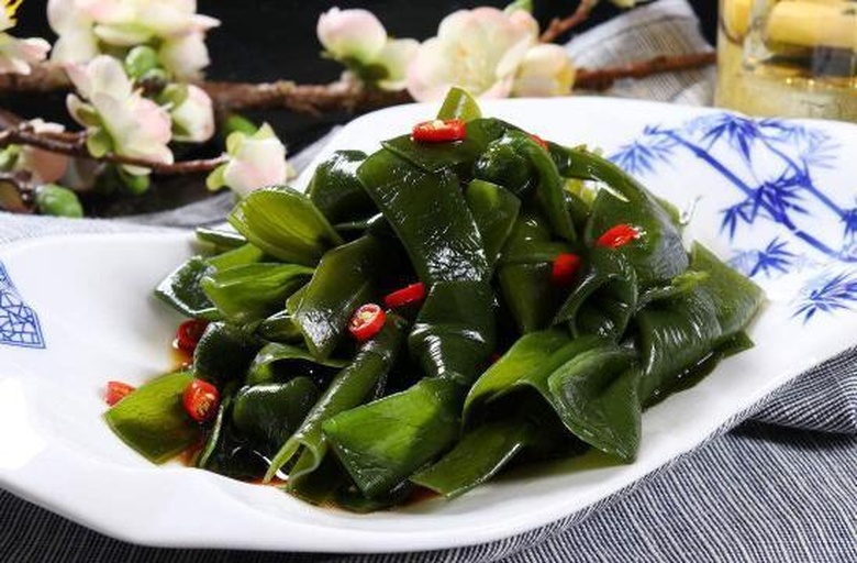 一碟凉拌海带丝，呈深褐色细条状，拌有蒜末、红油和香菜，装在白色圆盘中