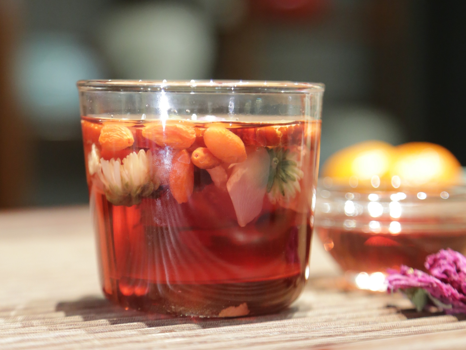 一位中年女性坐在阳台藤椅上,手持陶瓷杯饮用刚煮好的野菊花艾草水,杯子上方飘出淡淡热气,桌上放有药材包装袋与笔记本记录饮用感受,窗外阳光柔和,营造出自然健康的养生生活氛围 家庭饮用场景图