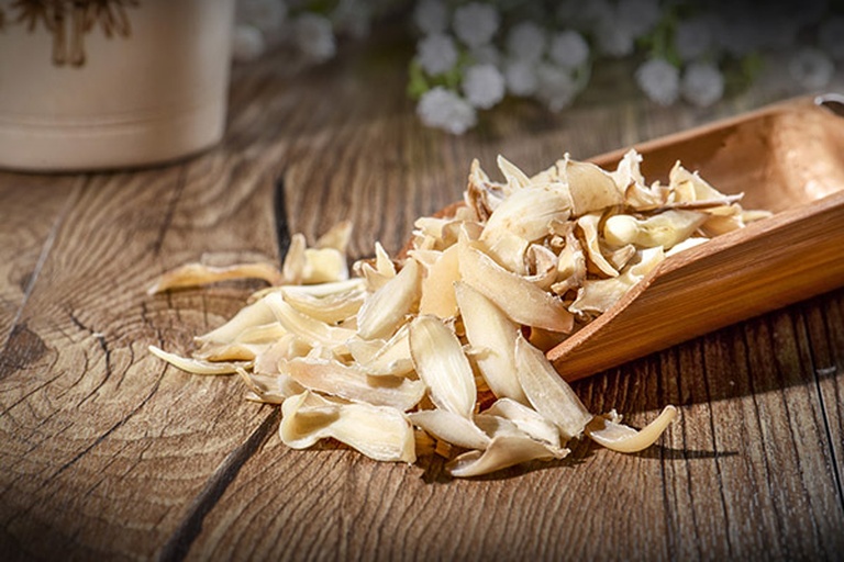 高清俯拍图:左侧为完整展开的淡黄色椴木银耳干品,质地厚实有光泽;右侧为白色片状干百合,边缘略卷曲,背景为原木色托盘,旁边放置不锈钢小勺和玻璃碗,营造自然健康的食材展示氛围 银耳与百合干品对比图