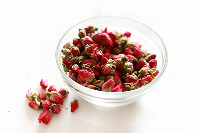 玻璃罐中分别盛放深红色食用玫瑰干花、玫瑰花蕾、玫瑰酱、玫瑰饼切片,背景为玫瑰种植基地航拍图,体现从田间到餐桌的产业链 食用玫瑰深加工产品展示