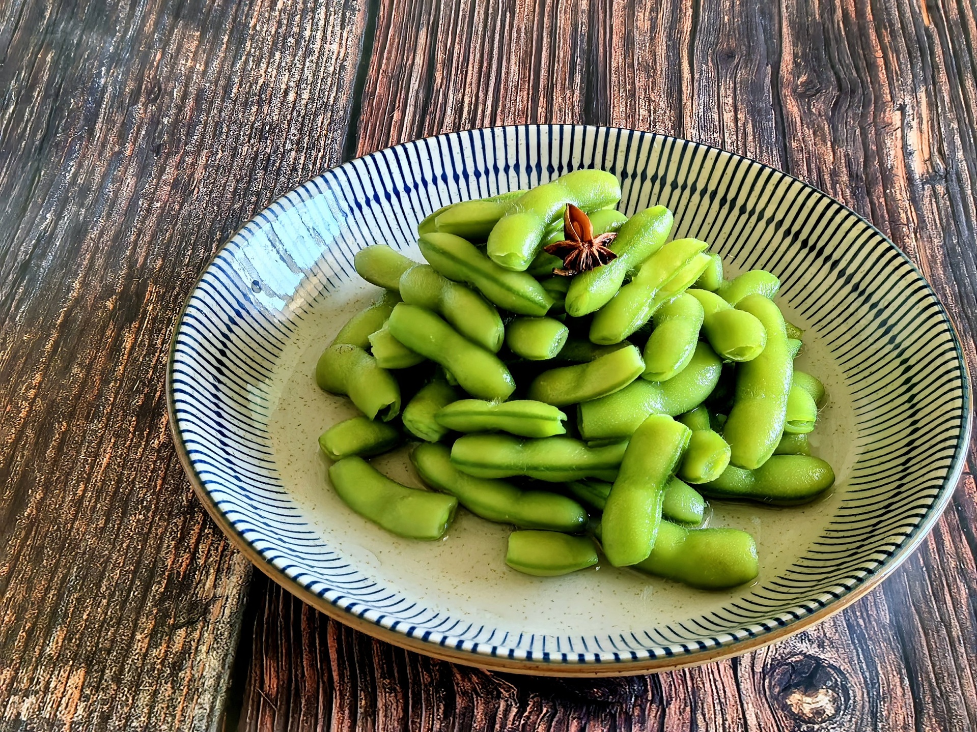 一组摆放在木质桌面上的即食毛豆系列产品,包括真空袋装、小盒分装和罐装口味款,包装设计清新自然,部分袋子打开露出翠绿的毛豆,旁边配有筷子和柠檬片,营造出休闲食用场景 包装精美的即食毛豆产品展示