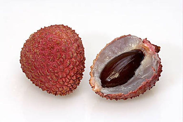 切开的南红荔枝展示内部结构:白色半透明果肉包裹着棕黑色种子,果肉质地紧实有光泽;旁边放置一把不锈钢水果刀,背景为木质砧板和绿叶衬托 南红荔枝剖面图