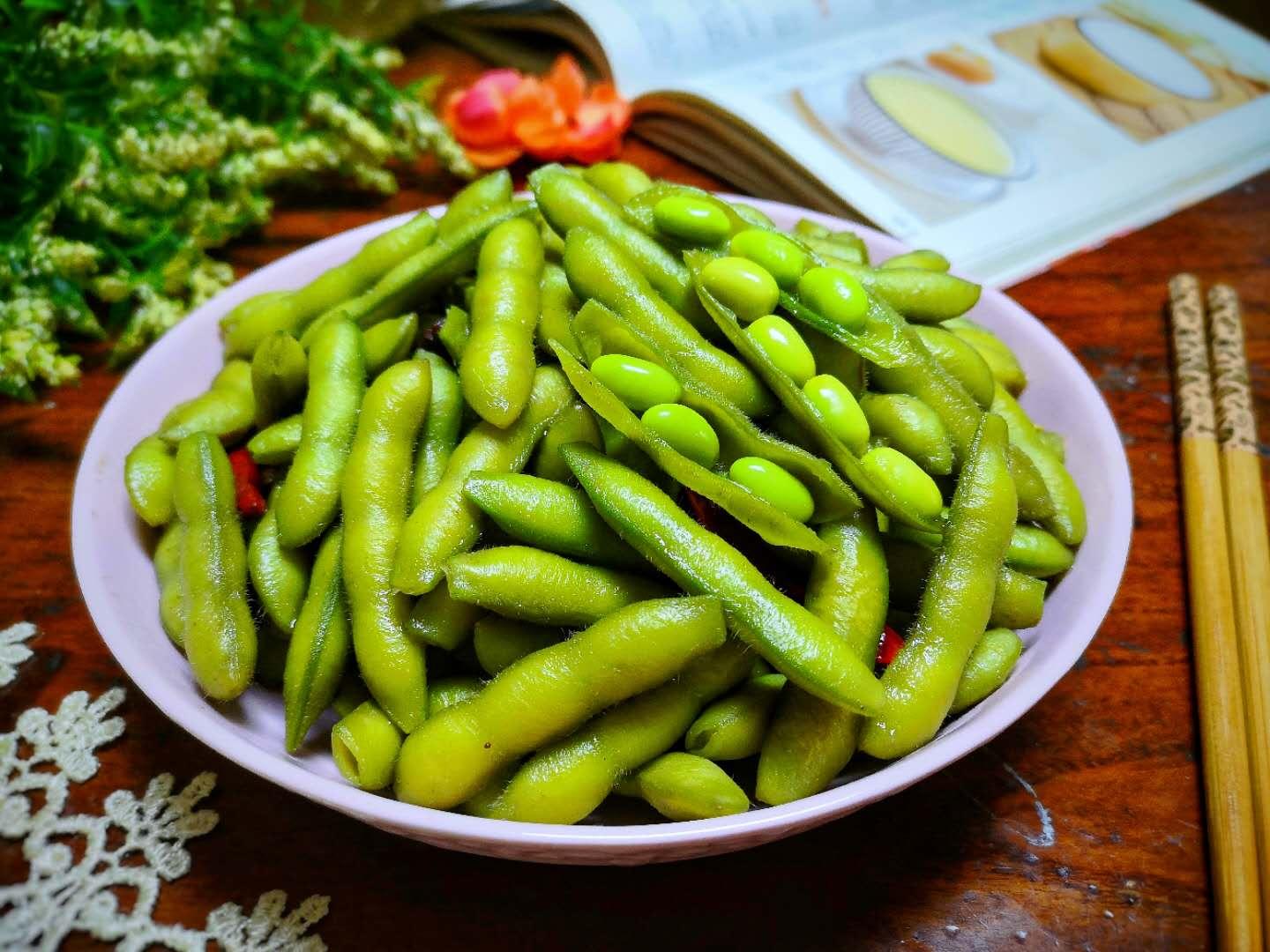 新鲜毛豆米与整只小公鸡并列摆放于木质案板上,背景为厨房环境,左侧是剥好的翠绿色毛豆仁,右侧是处理干净的小公鸡块,周围点缀姜片、葱段、干辣椒和香料 毛豆米与小公鸡原材料摆盘图