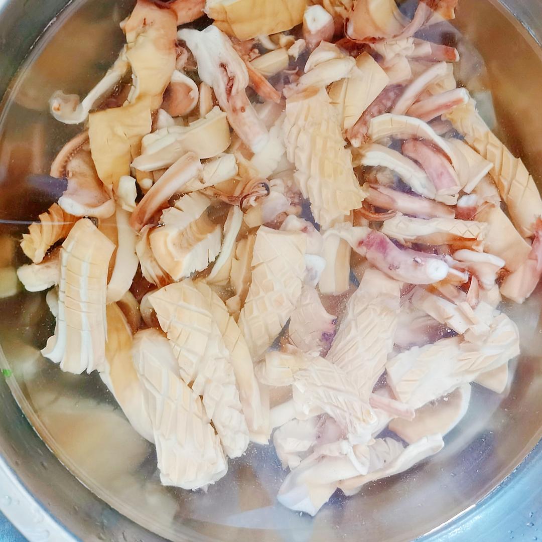 一名厨师正在清洗整只新鲜鱿鱼,背景为厨房操作台,鱿鱼呈乳白色带淡蓝光泽,表面湿润有光泽,内脏已去除,触腕完整,水槽中有流动清水冲洗残留黏液 新鲜鱿鱼与清洗处理过程