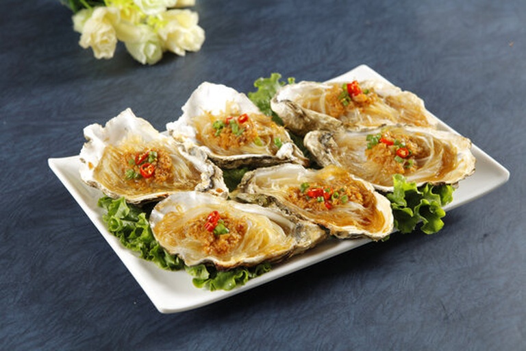 蒜蓉粉丝蒸生蚝组装过程:厨师正用食品级不锈钢夹子将65℃恒温预熟的生蚝肉整齐摆放在泡发粉丝上,右侧小碟盛放自制蒜蓉酱,背景可见新鲜香菜末和红小米辣圈 厨师手持夹子将65℃预熟的生蚝肉轻放在铺满粉丝的蒸盘上,旁边备好金黄蒜蓉酱和香菜末