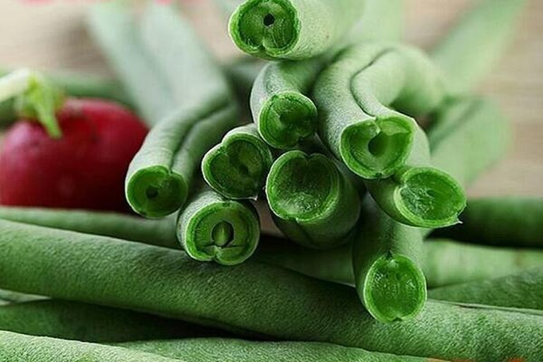 豆角预处理特写：新鲜翠绿豆角斜切成菱形段，整齐铺在白色瓷盘中，背景为淡蓝色厨房台面，水珠晶莹可见
